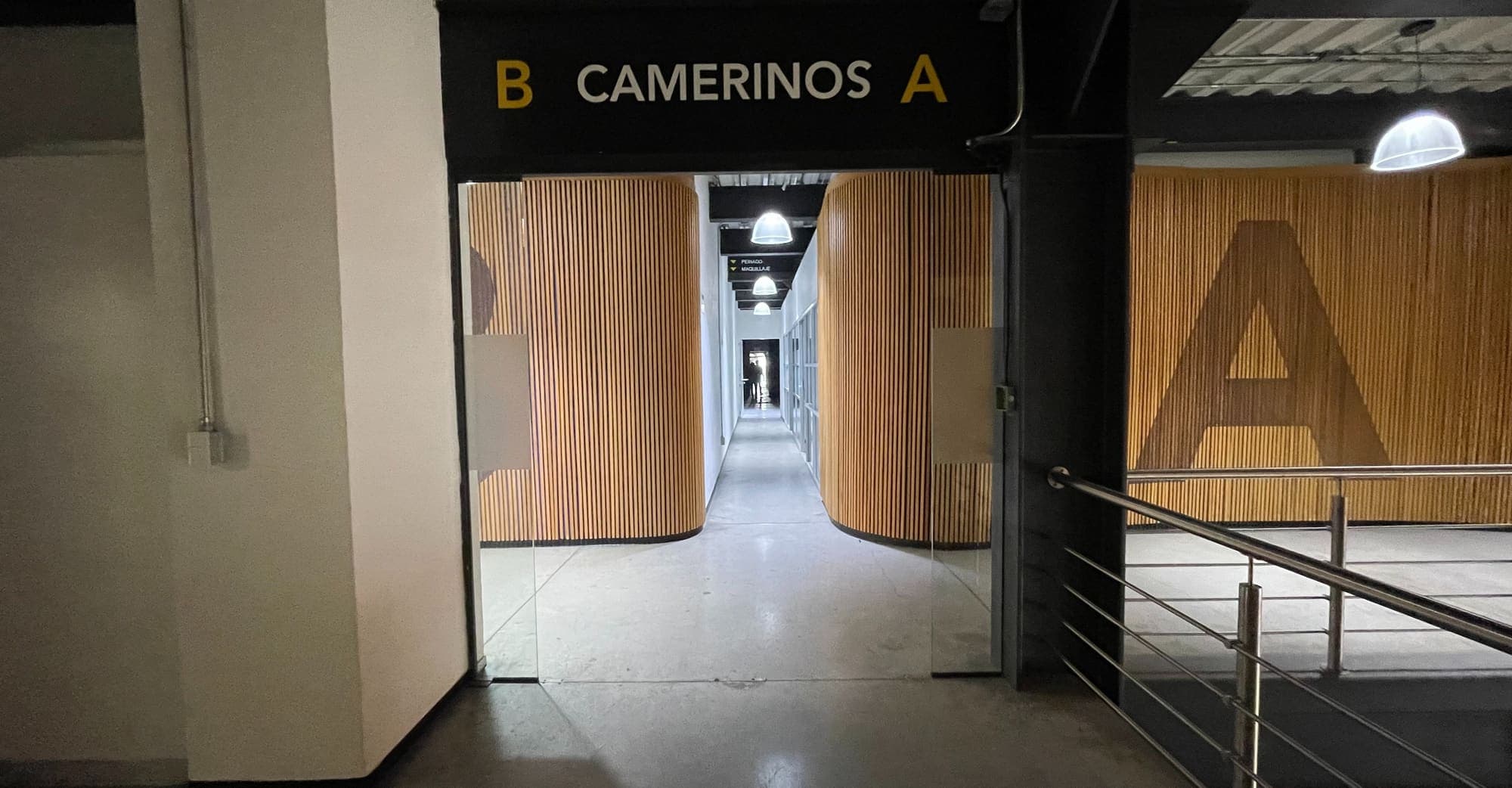 Acceso al pasillo de camerinos, rotulado «B Camerinos A», entre muros curvos de madera.