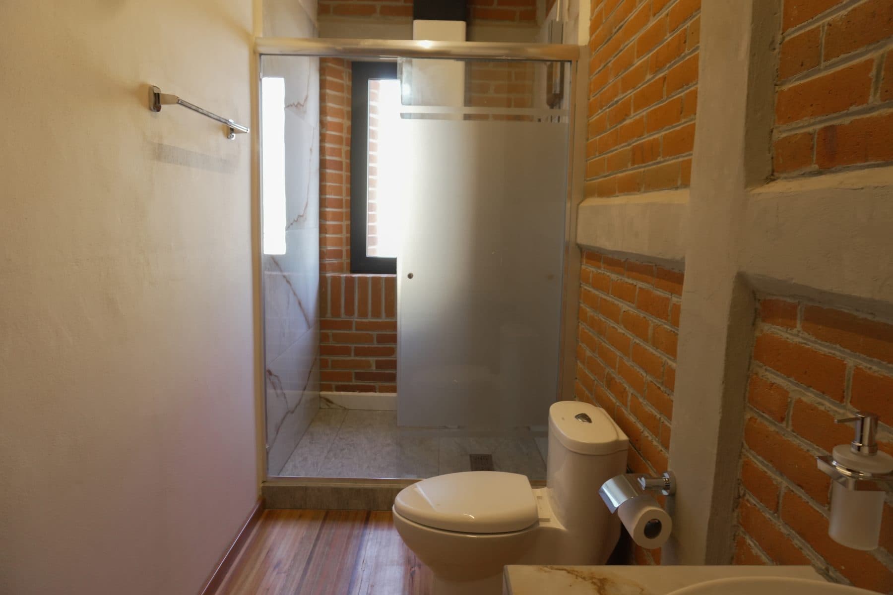 Baño de camerino con muro de ladrillo visto y regadera al fondo.
