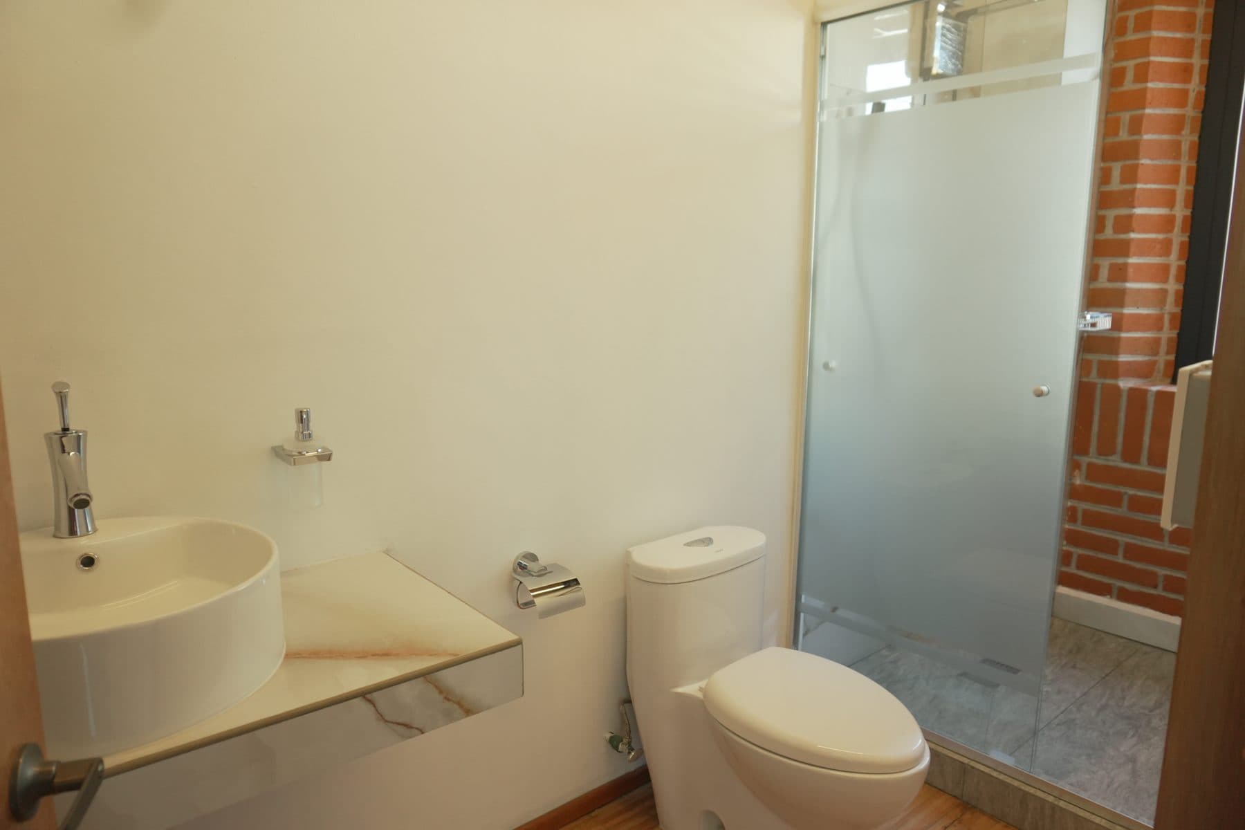 Baño de camerino con lavabo de sobreponer y regadera cerrada con cancel de cristal.
