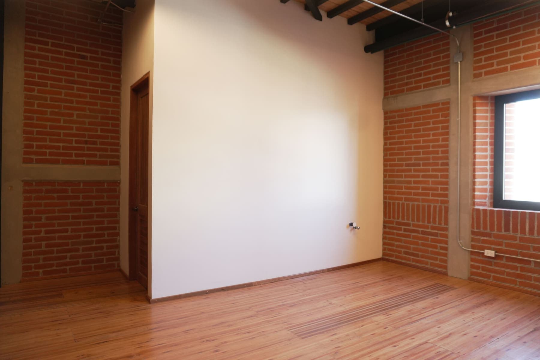 Camerino con ventanas al muro de ladrillo y viguería de madera a la vista en el techo.