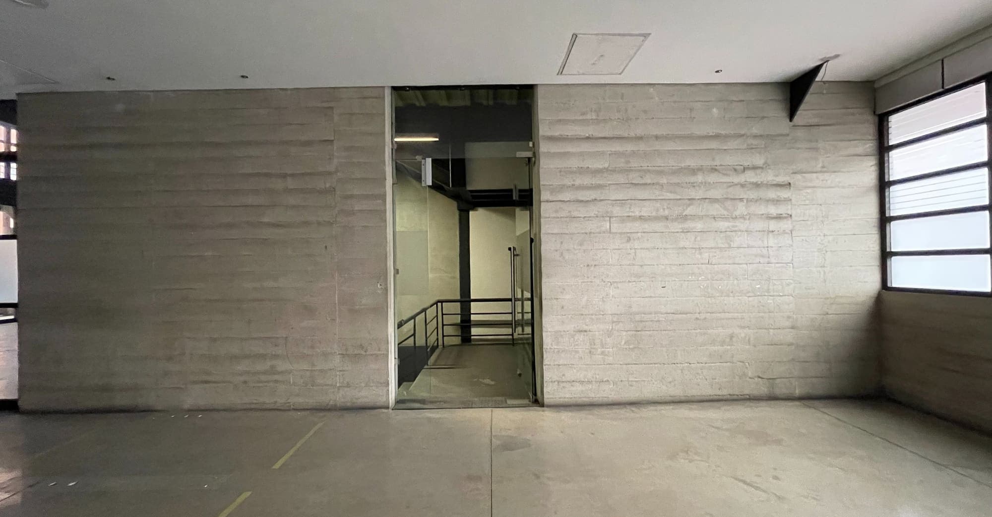Muro de concreto aparente con el paso hacia la escalera y los elevadores.