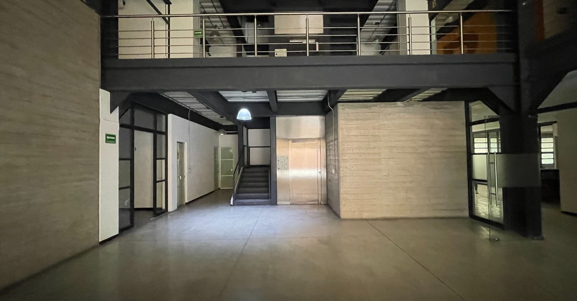 Vestíbulo de doble altura con escalera metálica y mezzanine de barandal.