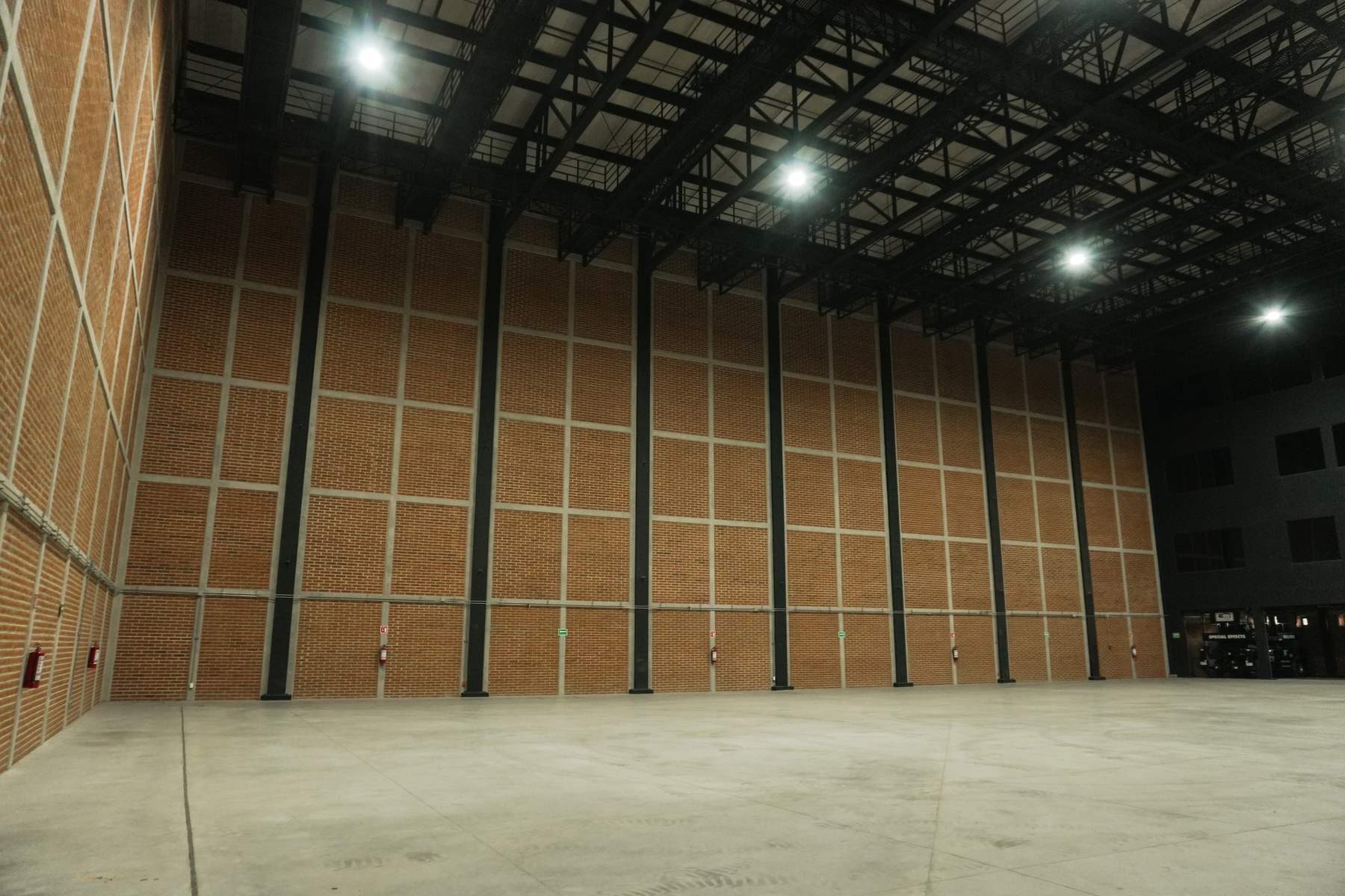 La nave a lo ancho: retícula de concreto sobre ladrillo hasta la estructura y luminarias colgadas de la parrilla.