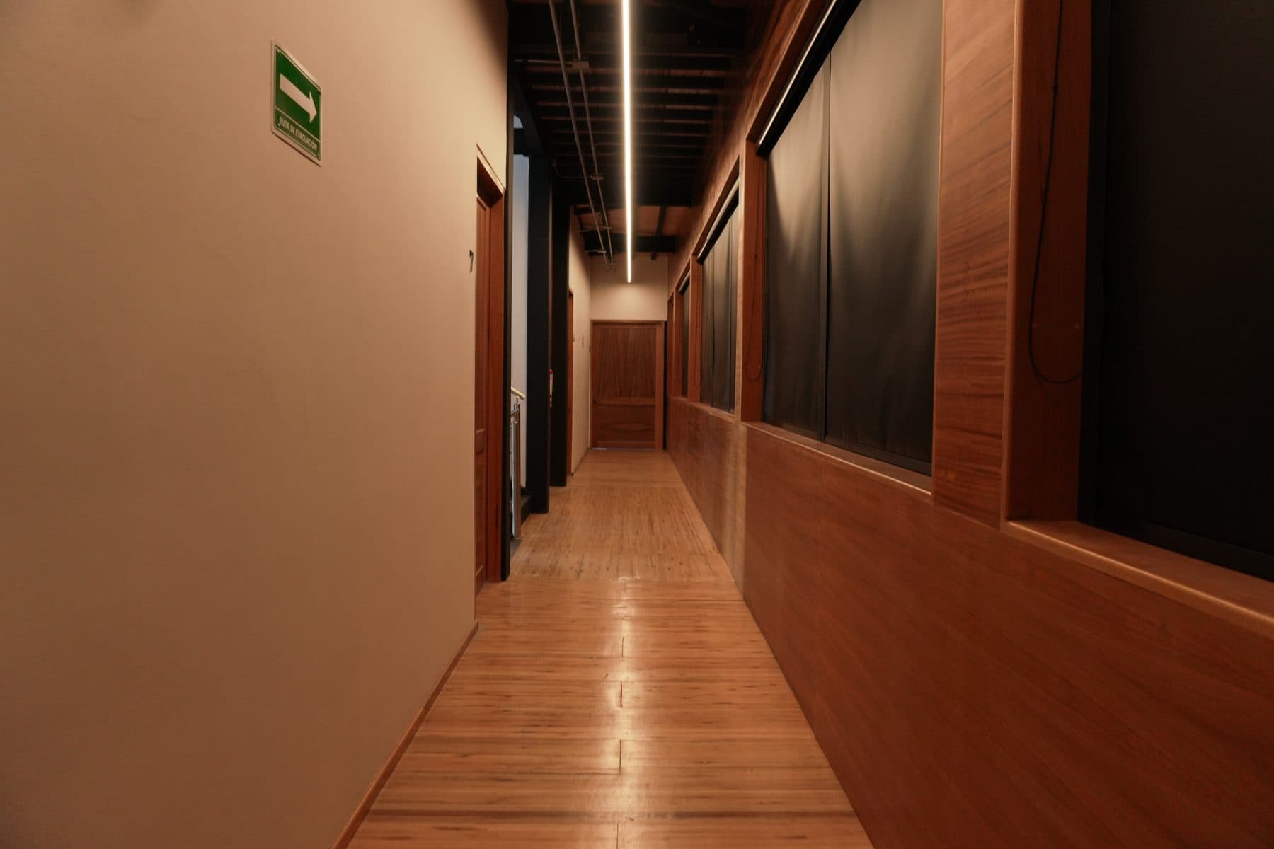Pasillo largo de piso de duela, con lambrín de madera a media altura y luminaria lineal corrida en el techo.