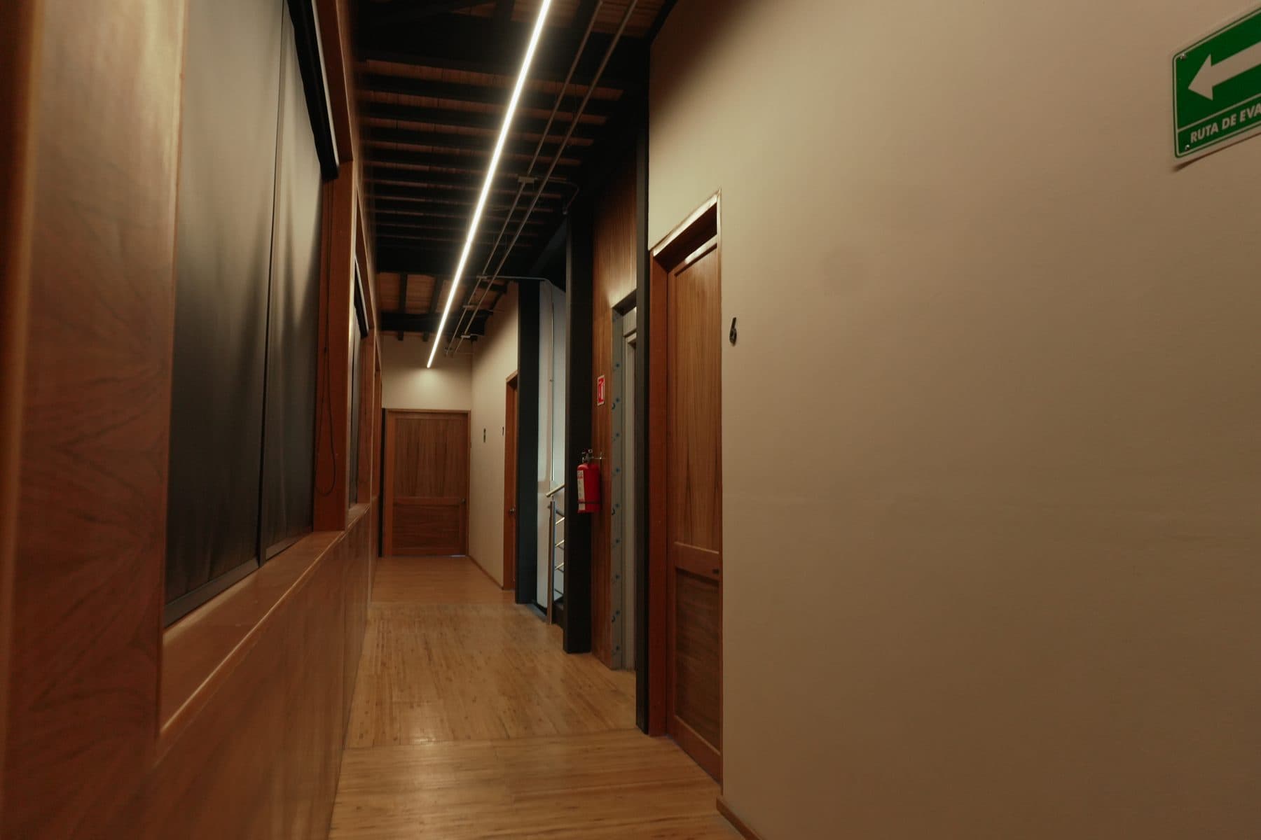 Pasillo con puertas de madera a un costado y lambrín oscuro al otro.