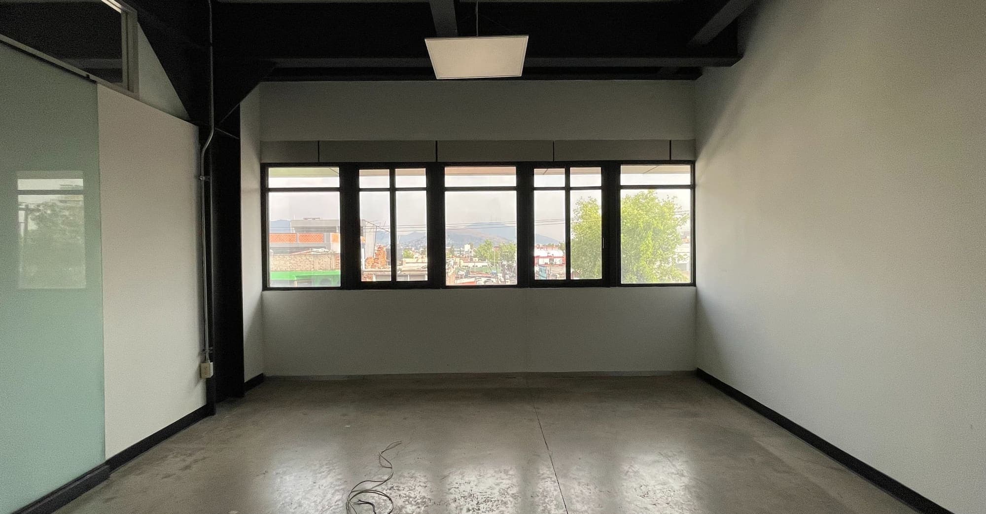 Oficina vacía con ventanal corrido y muro de vidrio a un costado.