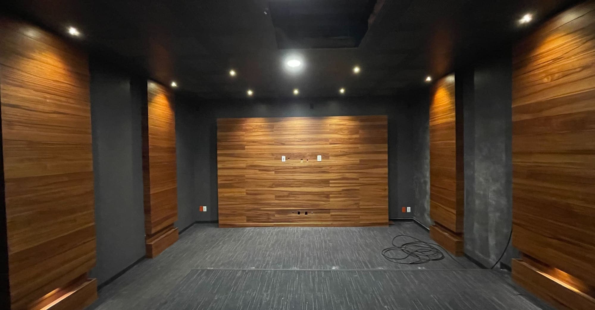 La misma sala oscura hacia el muro de madera, con alfombra y luz empotrada.