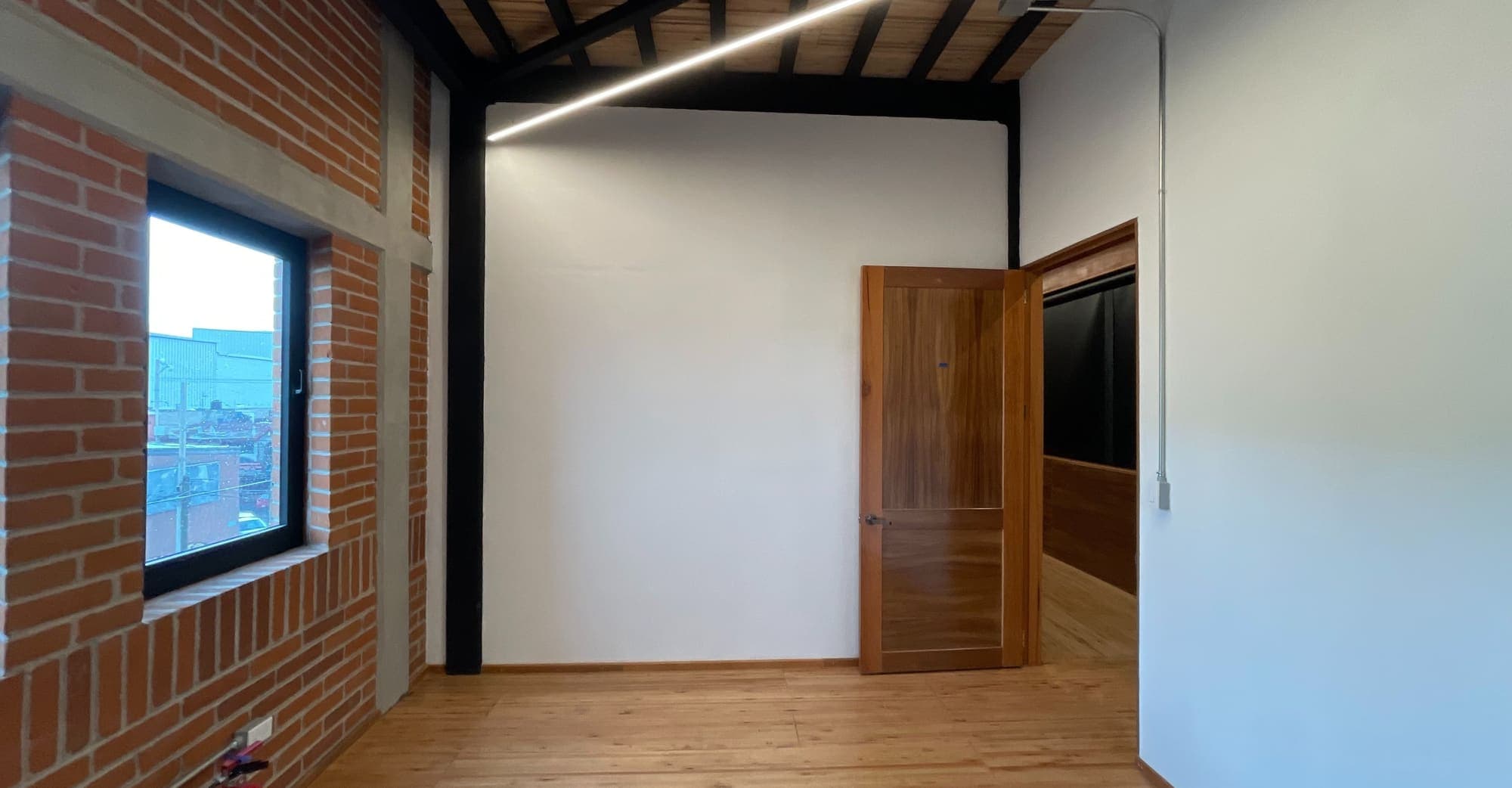 Sala de muros blancos y ladrillo, con ventana y puerta de madera.
