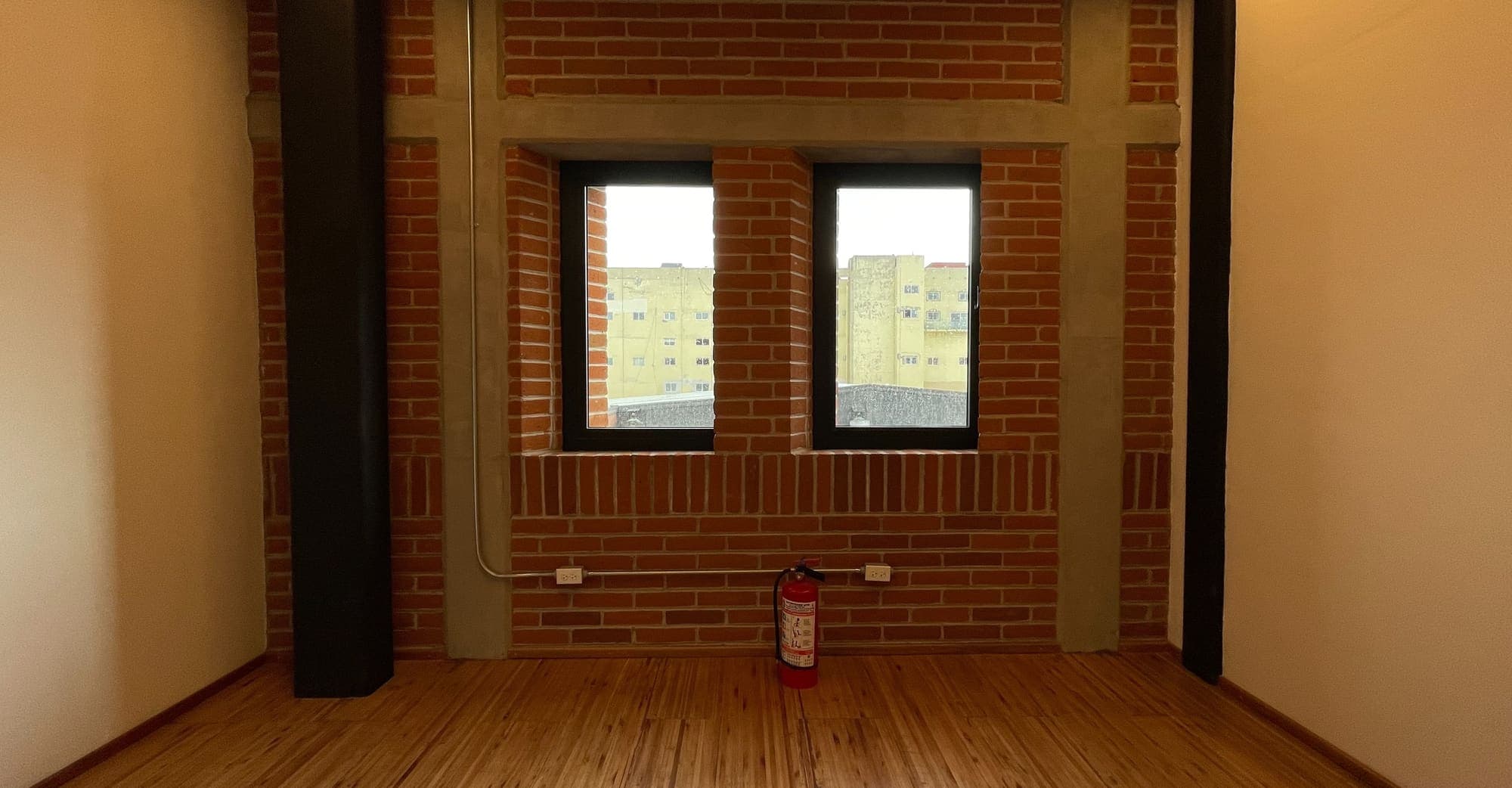 Sala de duela con muro de ladrillo y dos ventanas, entre columnas oscuras.